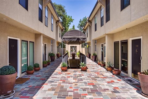 A long, narrow walkway with potted plants on either side leads to a covered patio area.