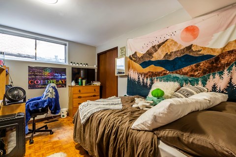 A bedroom with a bed, a chair, a desk, and a poster on the wall.