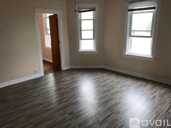 A room with wooden flooring and two windows.