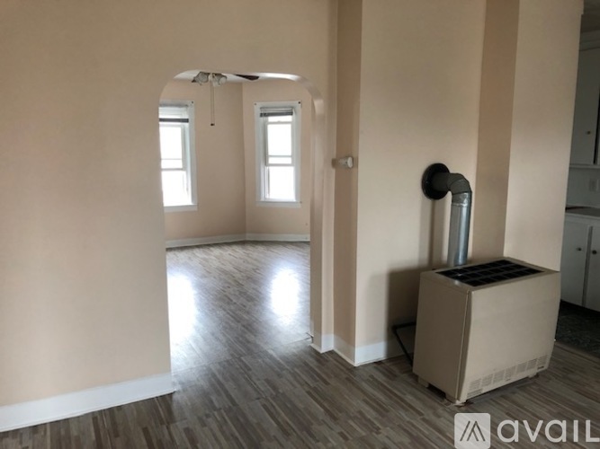 A room with a fan, a radiator, and a doorway leading to another room.
