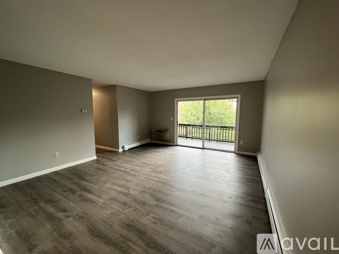 A spacious room with wooden flooring and a sliding glass door leading to a balcony.