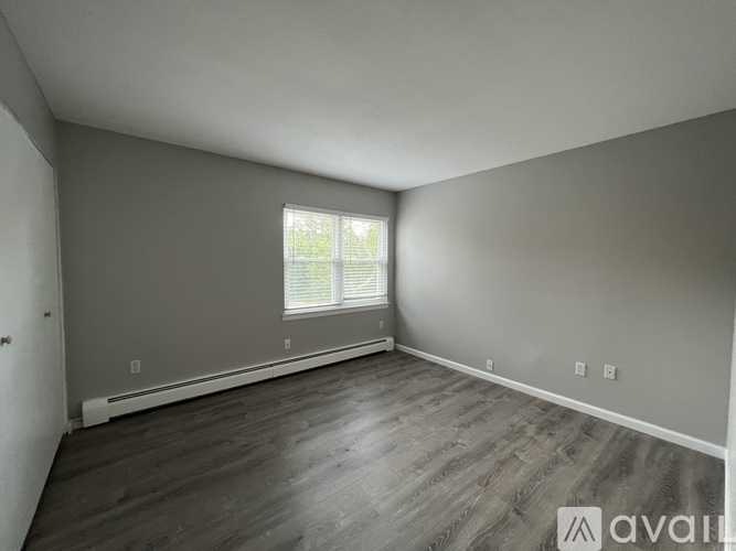 A spacious room with wooden flooring and a window with blinds.
