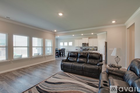 A living room with a black leather couch and a rug.