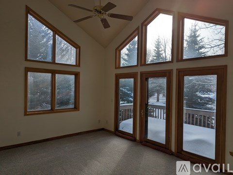A room with a ceiling fan and large windows showing a snowy landscape outside.