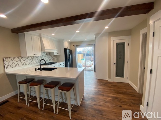 A kitchen with white cabinets and a white island with three stools.