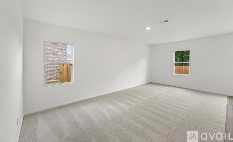 A spacious room with a carpeted floor and two windows.