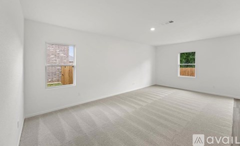 A spacious room with a carpeted floor and two windows.