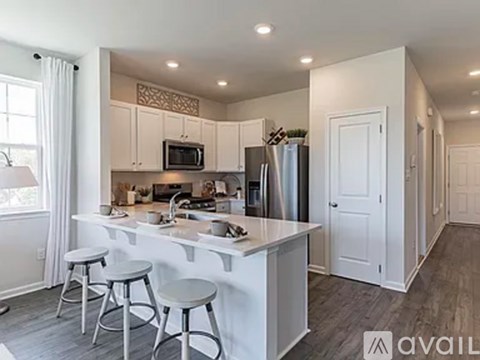 A kitchen with white cabinets and a white island with three stools.