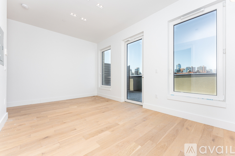 A spacious room with wooden flooring and large windows showing an urban landscape.