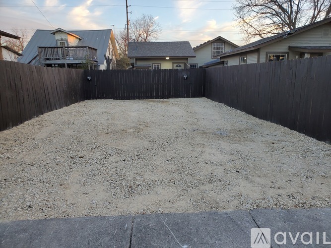 A backyard with a sandy area and a wooden fence.