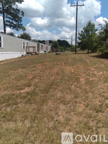 A grassy field with a few houses and trees in the background.