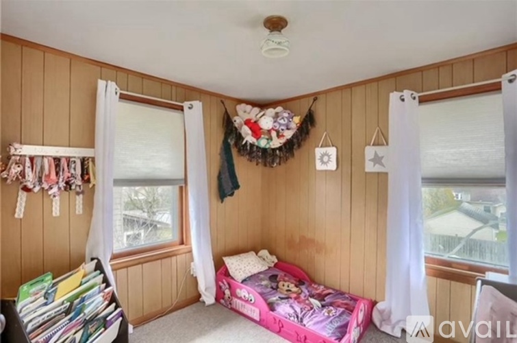 A child's bedroom with a pink bed and a window with curtains.