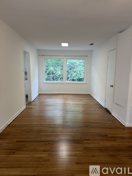 A room with wooden flooring and a window showing greenery outside.