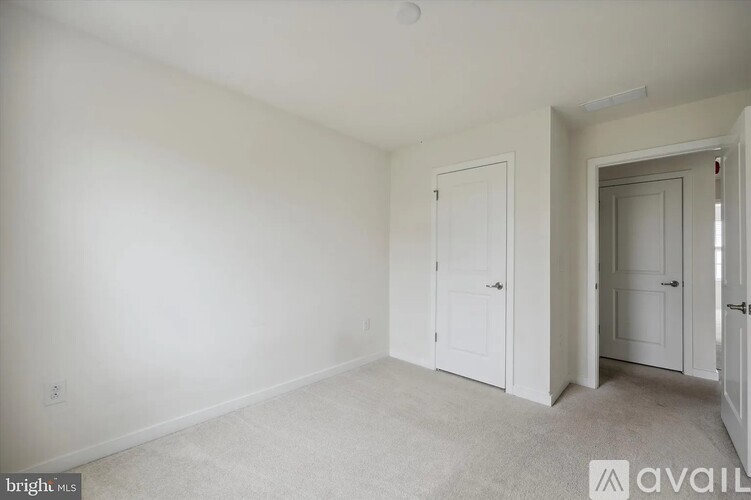 A white bedroom with two doors and a carpeted floor.