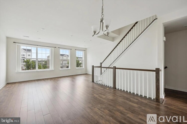 A spacious room with wooden floors and a staircase with white railings.