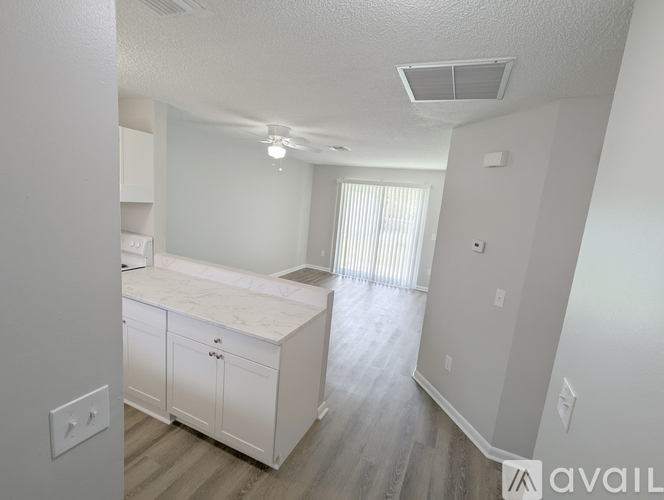 A white kitchen with a marble countertop and wooden flooring.