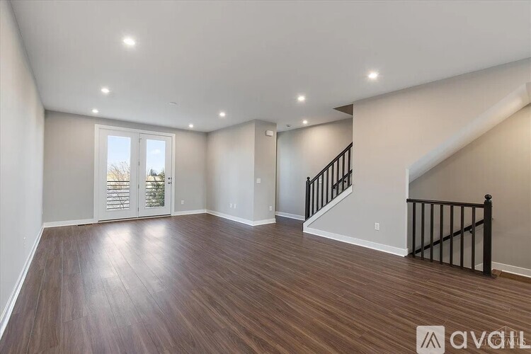 A spacious room with wooden floors and a staircase with a black railing.