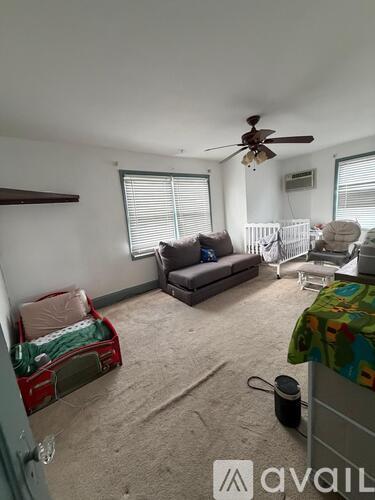 A living room with a couch, a fan, and a window with blinds.