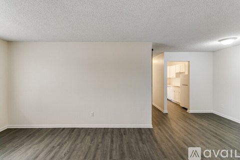 A room with wooden flooring and white walls, with a doorway leading to another room.