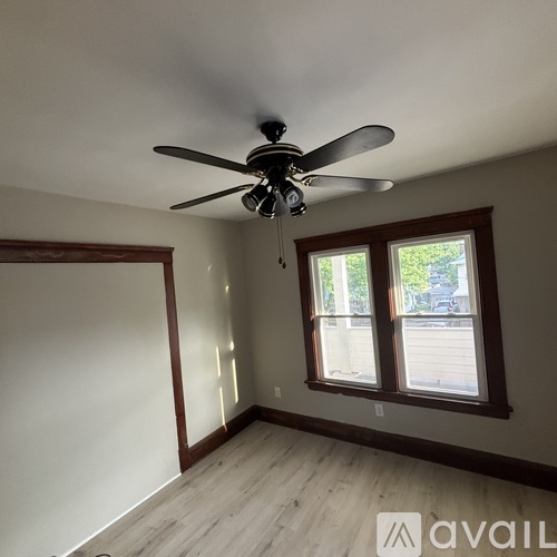 A room with a ceiling fan and two windows.
