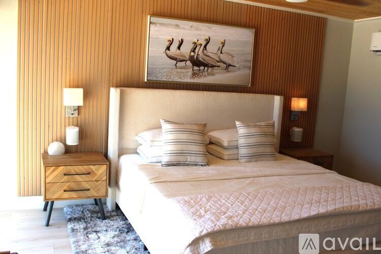 A bedroom with a large bed and a painting of two birds on the wall.