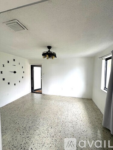 A room with a clock on the wall and a window with curtains.