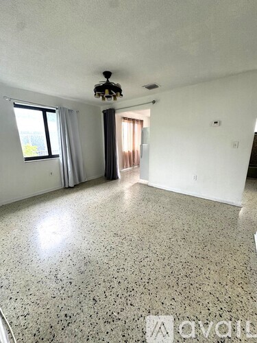 A spacious room with a speckled floor and a window with curtains.