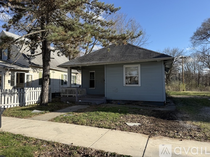 A small house with a grey roof and a white picket fence.