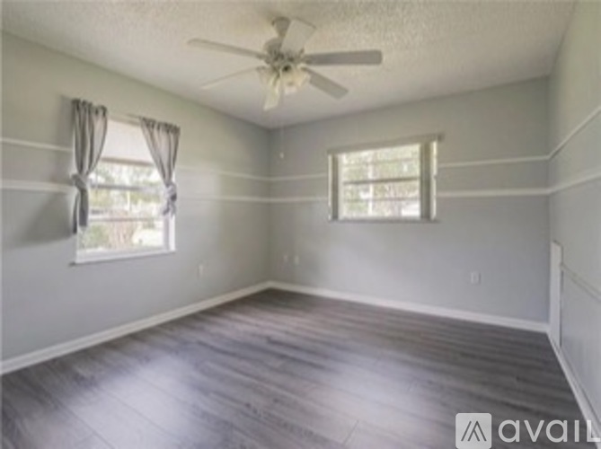 A room with a ceiling fan and two windows.