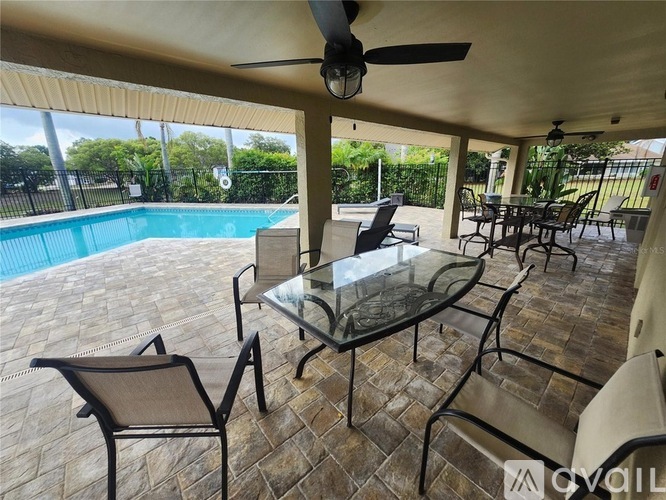 A patio with a glass table and chairs and a pool in the background.
