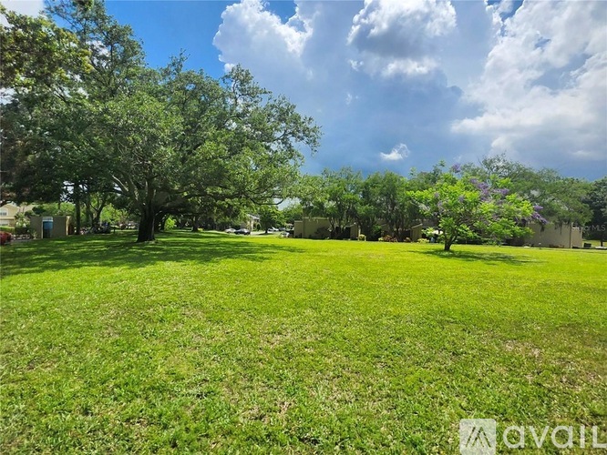 A grassy field with trees and a cloudy sky.