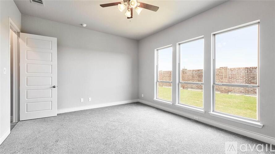 A spacious room with a ceiling fan and large windows overlooking a brick wall.