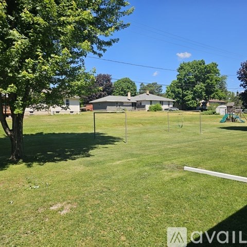 A grassy field with a tree and a house in the background.