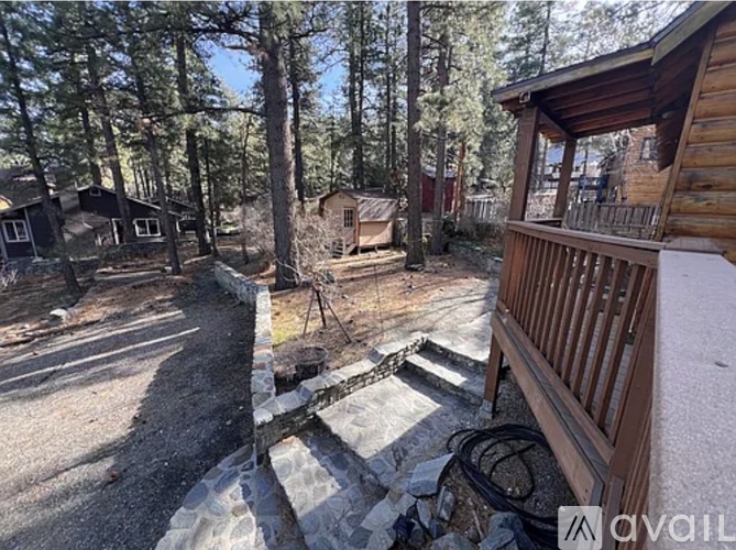 A wooden cabin is surrounded by trees and has a stone wall and steps leading to the front door.