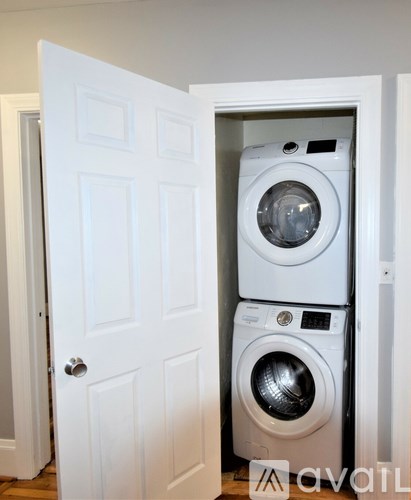 A white door is open to reveal a stack of white washing machines.