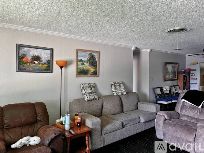 A living room with a brown leather chair, grey couch, and a painting on the wall.