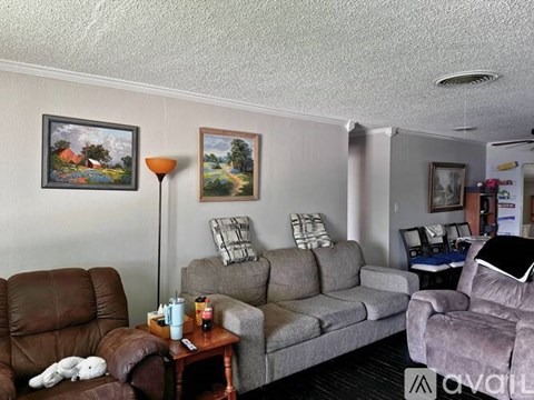 A living room with a brown leather chair, grey couch, and a painting on the wall.