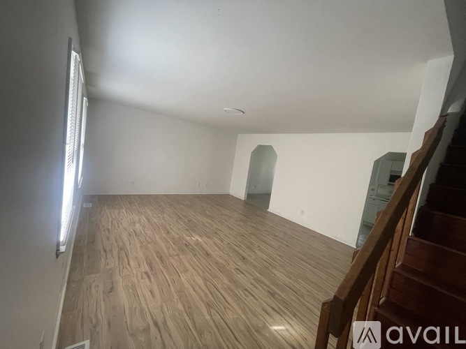 A room with wooden flooring and a staircase on the right side.