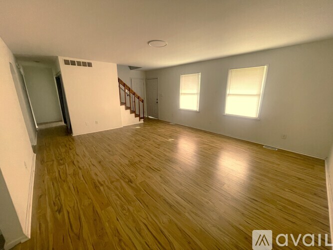 A spacious room with wooden flooring and two windows.