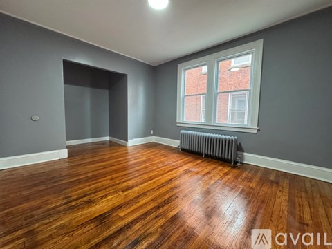 A room with wooden floors and a window with a radiator beneath it.