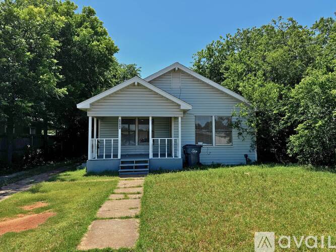 A house with a porch and a trash can in front.