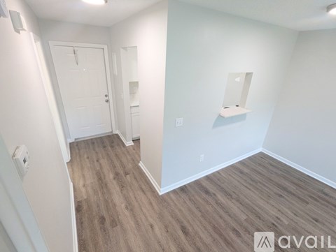 A room with wood flooring and white walls, with a door and a mirror on the wall.