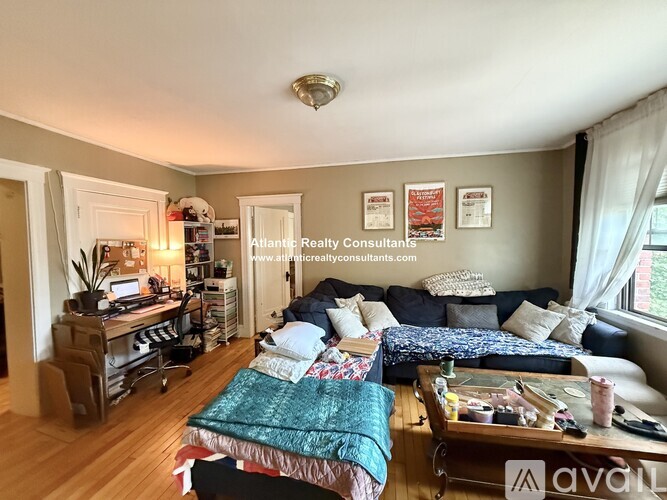 A living room with a couch, a coffee table, and a bed with a green blanket.