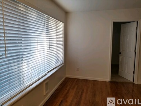 A room with a window covered by white blinds and a door on the right side.