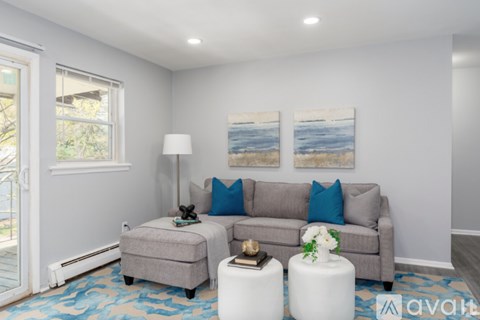 A living room with a grey couch, a small ottoman, a table with a vase of flowers, and two paintings on the wall.