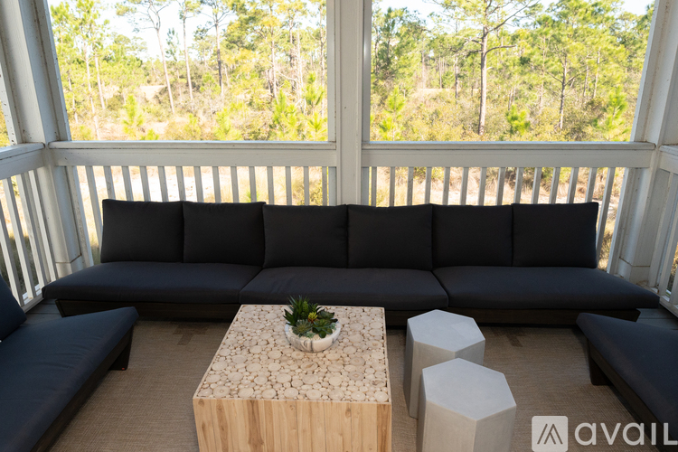 A black sectional sofa with a wooden coffee table in front of a window with a view of trees.