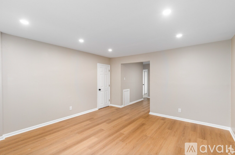 A spacious room with wooden flooring and white walls.
