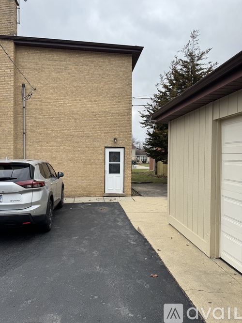 A white car is parked in front of a brick house.