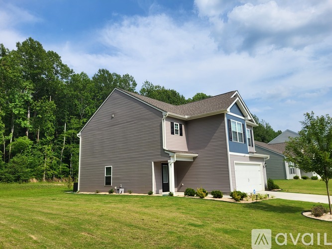A house with a grey siding and a white garage door is surrounded by greenery.