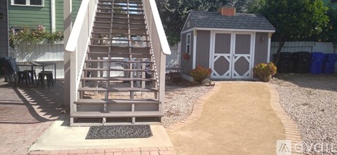 A wooden staircase with a metal grate at the bottom leads up to a small white building.